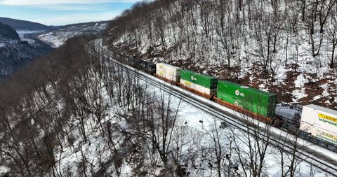 Altoona , PA , United States - 01 22 2022: Rail logistics, train travel. Diesel locomotive with JB Hunt Intermodal container shipment in winter snow mountain pass.