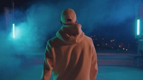 Back of hiphop stylish bboy dancing guy in yellow outfit walking outside on night stage rooftop and watching cityscape. Artisy performance. Nightlife. - Powered by Shutterstock - Get 15% off with code: PIKWIZARD15