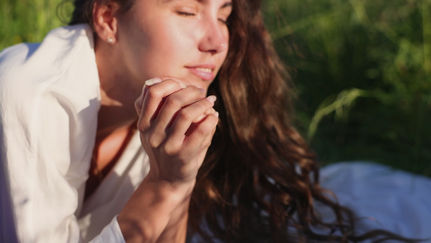 Attractive brunette girl in a white blouse stands in the middle of a field of lupines. The pleasure and relaxation of nature. Shadows from the grass fall on her face.