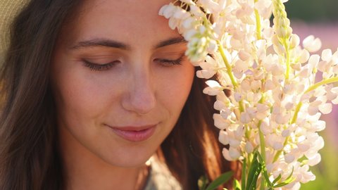 Portrait of an attractive brunette woman with white lupine flowers. Positive emotions and enjoyment of nature. Inhaling the fragrance of flowers. Getting rid of allergies