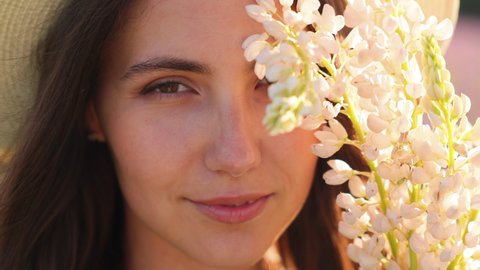 Portrait of an attractive brunette woman with white lupine flowers. Positive emotions and enjoyment of nature. Inhaling the fragrance of flowers. Looking into the camera