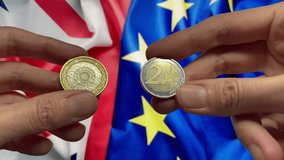 2 Pound and 2 Euro coins in hands on background of the UK and European Union flags. United Kingdom after Brexit. Money rate. Currency, money exchange concept. 4k video - Powered by Shutterstock - Get 15% off with code: PIKWIZARD15