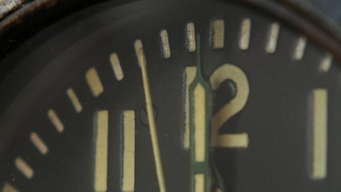 Extreme close-up of the dial of a vintage aviation clock. The arrows show almost noon (midnight). The seconds are ticking, approaching 12 o'clock.	
