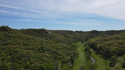 Scenic valley with golf course at the bottom. Trees covering the sides of the hills with rock outcroppings. Clear blue sky with wispy clouds. 