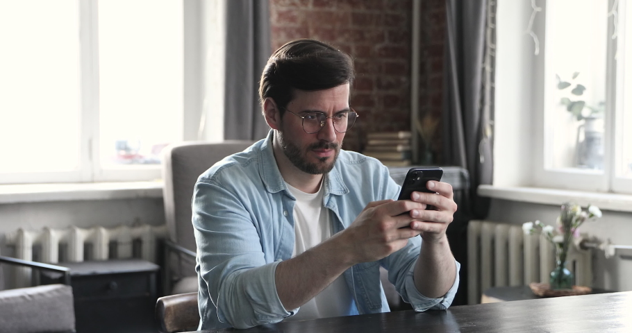 Frustrated and young man in glasses user feel angry dissatisfied with incorrect slow software work. Irritated guy user scolding broken modern phone detecting malware Royalty-Free Stock Footage #1086847121