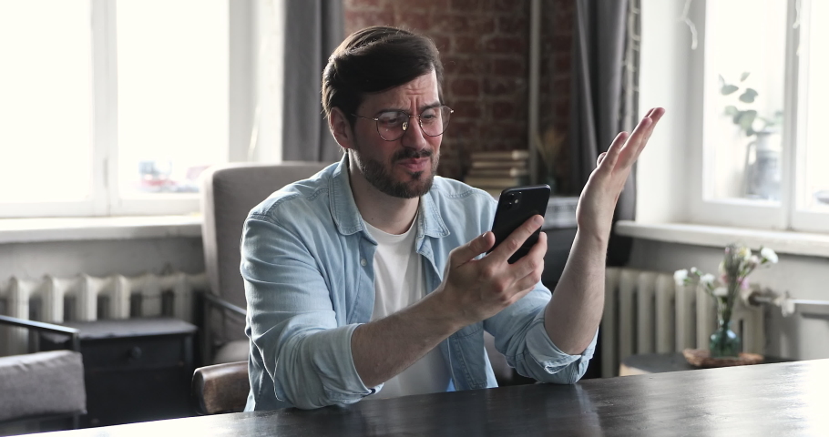 Frustrated and young man in glasses user feel angry dissatisfied with incorrect slow software work. Irritated guy user scolding broken modern phone detecting malware | Shutterstock HD Video #1086847121