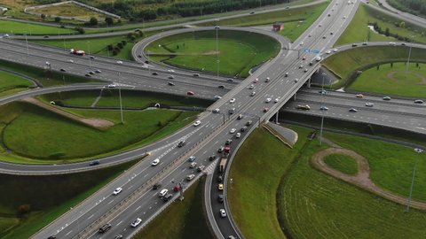 Highway multilevel traffic overpass intersection with driving automobiles among green meadows on city outskirts aerial panorama