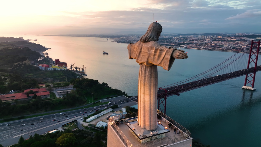 Drone flight around the statue of Jesus Christ in Lisbon. Jesus monument in sunset light. The god statue over the night landscape. Jesus protecting Portugal people.