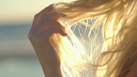 Portrait of a blonde at sunset on the ocean. Sexy girl looking at the camera slow motion touches her hair