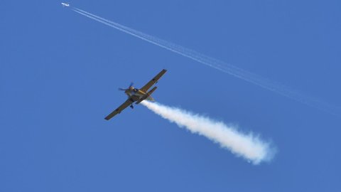 Thiene Vicenza Italy OCTOBER, 16, 2021 Small yellow aeroplane performs aerial acrobatics against the clear blue sky. A line of white aerobatics smoke behind the vehicle. Mudry CAP 231 in slow motion