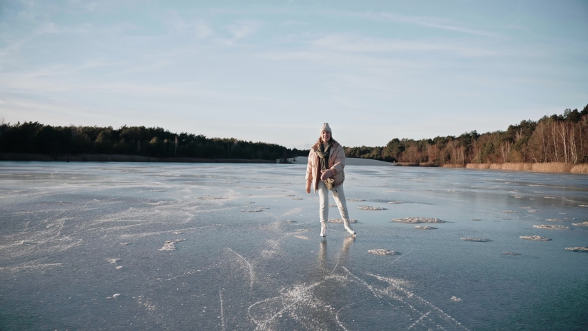 Woman ice skating on a frozen lake on a sunny winter day approaching the camera. Sunny ice skating day in beautiful landscape. Girl in white skates on blue lake. High quality 4k footage