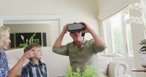 Happy senior caucasian couple with grandson using vr headset in living room. family spending time together at home.