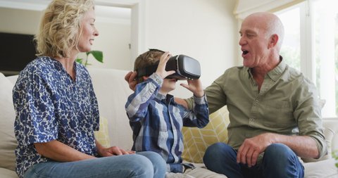 Happy senior caucasian couple with grandson using vr headset in living room. family spending time together at home.