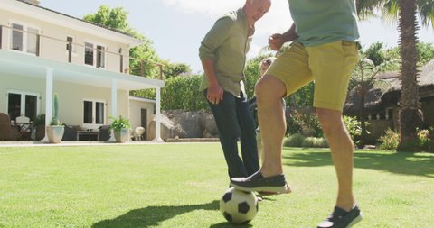 Happy caucasian grandfather with adult son and grandson playing football in garden. family spending time together at home.