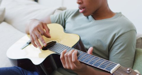 Happy african american man plays guitar and singing at home. leisure time, relaxing at home alone.