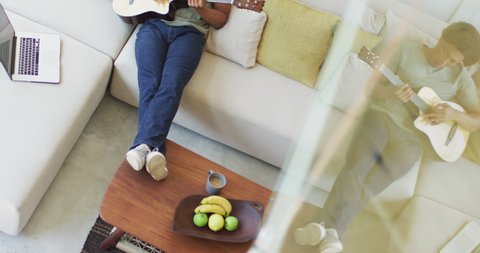 African american man plays guitar and singing, using laptop at home. leisure time using technology, relaxing at home alone.