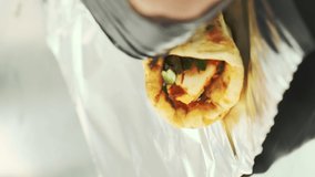 The chef's hands in gloves wrap the tortilla with meat in foil. Street food, fast food, takeaway. Vertical video

