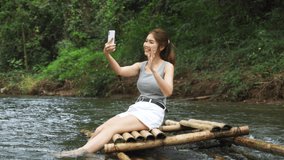 Young asian woman sitting on a bamboo raft making a video call , vlog   using smartphone.