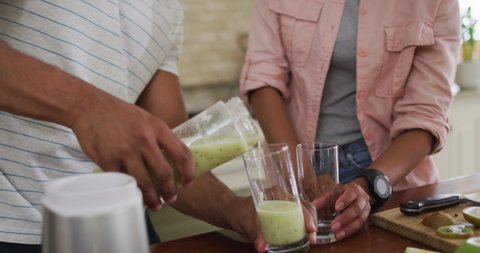 Hands of biracial couple in kitchen preparing smoothie, pouring it into glass. healthy lifestyle and enjoying quality leisure time at home.