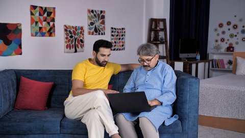 An elderly old man and his young son in discussion working on laptop - new age device use. Two different generations use a laptop together - electronic device, family bonding, internet access