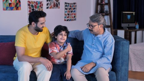 Handsome father and an old man hugging an adorable child at home - three generations, Indian joint family, love and care. Grand father, son, and grandson spending time together - leisure time, fami...
