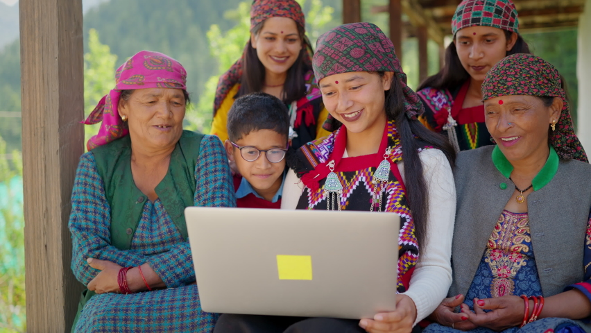 A cheerful Asian indian group of family members including women wearing traditional costumes and a kid sitting together using a laptop in a remote or rural area. Concept of distant communication. Royalty-Free Stock Footage #1086860849
