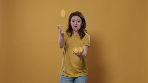Playful woman acting silly trying to juggle oranges being funny while dropping them in studio. Individuality concept of person with fun and goofy personality showing juggle talent.