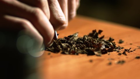 A man uses a knife and hands to prepare tobacco for a smoking. Close up.