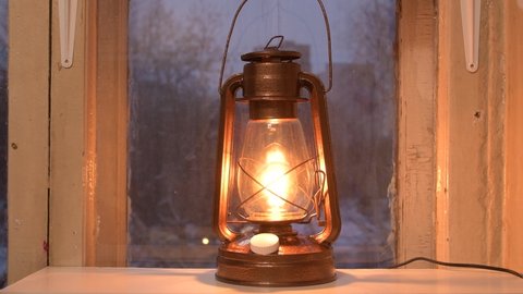An old oil lamp has been converted into a modern electric lamp with a dimmer. A kerosene lamp is on the window. The concept of reasonable consumption