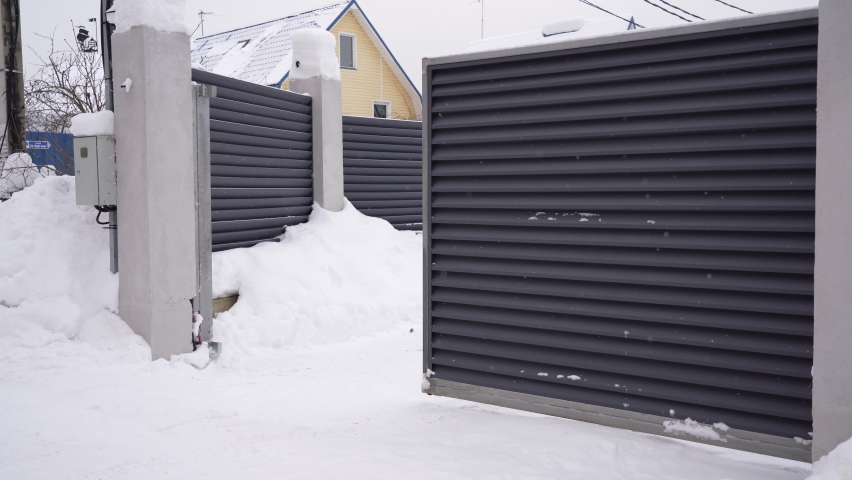 View of an automatic gate closing at snowy winter day. Modern design motorized automatic driveway gate, fence gate of courtyard of residential building in winter. | Shutterstock HD Video #1086866975