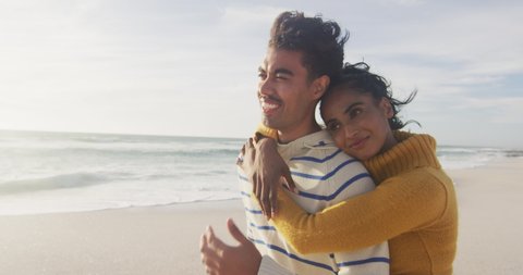 Portrait of smiling hispanic couple standing and embracing on beach. holidays, relaxation, outdoor lifestyle and togetherness.