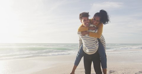 Happy hispanic man carrying piggyback woman and having fun on beach. holidays, relaxation, outdoor lifestyle and togetherness.
