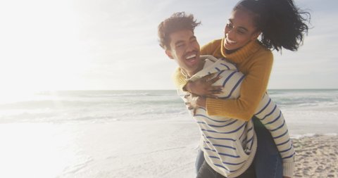 Happy hispanic man carrying piggyback woman and having fun on beach. holidays, relaxation, outdoor lifestyle and togetherness.