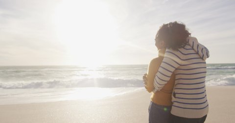 Back view of happy hispanic couple standing and embracing on beach. holidays, relaxation, outdoor lifestyle and togetherness.