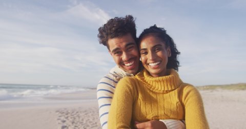 Portrait of happy hispanic couple standing and embracing on beach. holidays, relaxation, outdoor lifestyle and togetherness.