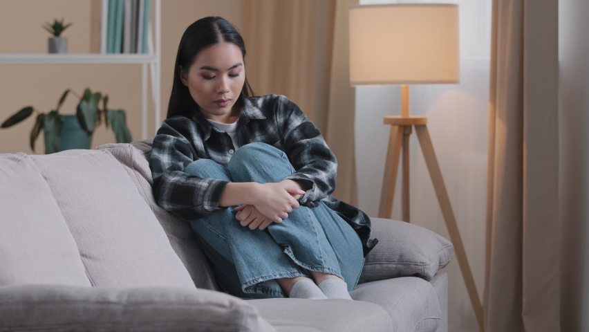 Sad worried asian korean woman having psychological problem sitting on sofa couch feeling alone anxiety depression japanese girl upset frustrated at home grief troubled unwanted pregnancy boredom | Shutterstock HD Video #1086871151