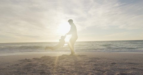 Hispanic father playing with son on beach at sunset. family holidays, free time, togetherness and spending time outdoors.