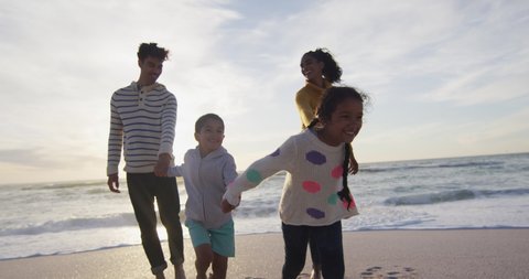 Happy hispanic familyholding hands and walking on beach at sunset. family holidays, free time, togetherness and spending time outdoors.