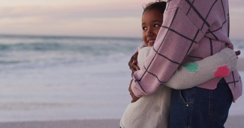 Midsection of hispanic mother embracing daughter on beach at sunset. family holidays, free time, togetherness and spending time outdoors.