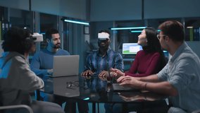 Diverse team of coworkers sitting around the table in evening office and working in virtual reality headset. Creative colleagues having meeting - Powered by Shutterstock - Get 15% off with code: PIKWIZARD15