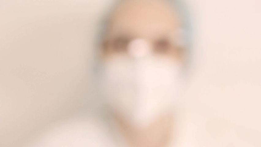 Extreme Close-up of a scientist, nurse or doctor in a white respirator, gloves and protective glasses, the developer of the coronavirus vaccine is holding a white transparent ampoule. The doctor looks Royalty-Free Stock Footage #1086874313