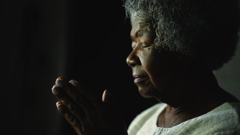 A spiritual older woman praying to God a senior African person prays