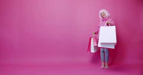 Happy Woman after shopping with colorful bags and her dog in pink colour concept. The woman enjoys the discount and the purchases made. smiling after successful shopping isolated on pink background
