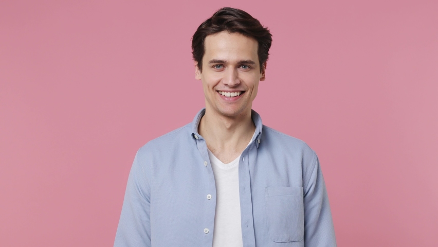 Happy blithesome charismatic fascinating fun young brunet man 20s years old wears blue shirt looking camera smiling isolated on plain pink background studio portrait. People emotions lifestyle concept Royalty-Free Stock Footage #1086876110
