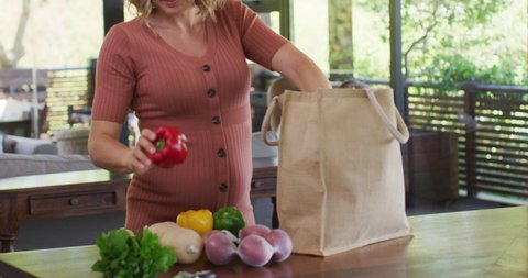 Caucasian pregnant woman unpacking bag of groceries in kitchen. expecting baby and healthy lifestyle during pregnancy.