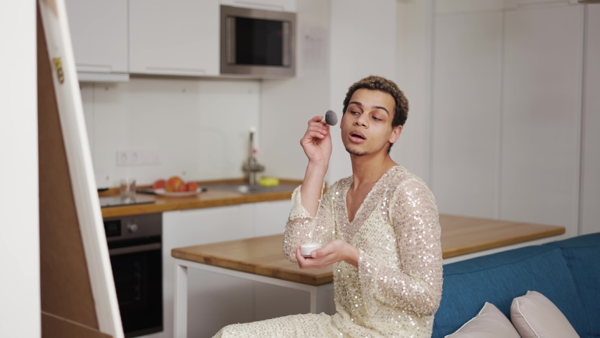 A transgender guy in fancy dress doing make up with brush and powder