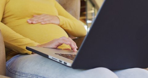 Midsection of caucasian pregnant woman sitting in armchair with laptop. pregnancy, motherhood, expecting baby and spending time at home.
