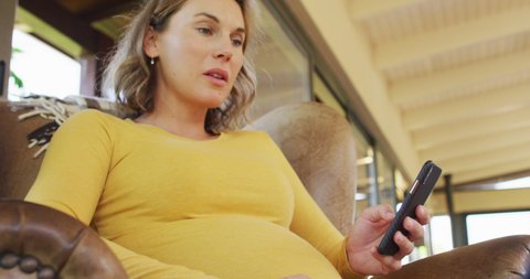 Caucasian pregnant woman sitting in armchair with smartphone. pregnancy, motherhood, expecting baby and spending time at home.