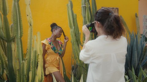 A beautiful black model poses for a photographer. Stylish fashion photo shoot in a cactus garden