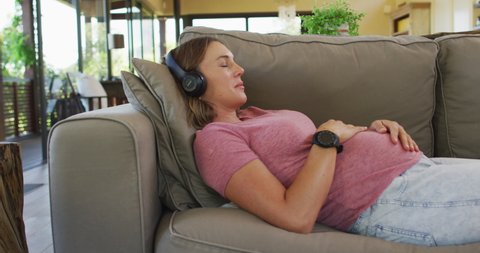 Relaxed caucasian pregnant woman lying on sofa and listening to music. pregnancy, motherhood, expecting baby and spending time at home.